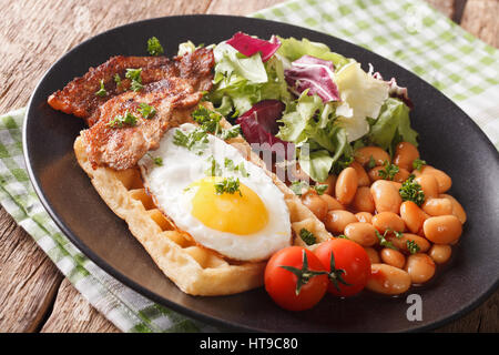 Breakfast with fried egg, waffles, bacon, mix lettuce and beans close-up on the table. horizontal Stock Photo