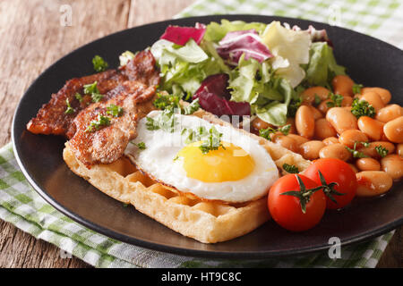 English breakfast with fried egg, waffles, bacon, salad and beans close-up on the table. horizontal