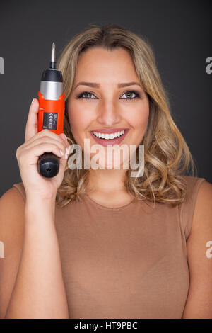 Young woman standing holding an electric screwdriver close to her head. Stock Photo