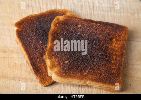Two slices of burnt toast on a wooden chopping board. Stock Photo