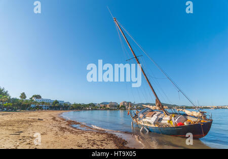 Abandoned & stranded, rusty old sail boat on the beach in Sant Antoni De Portmany. Warm sunny day in Balearic Islands, Spain. Stock Photo