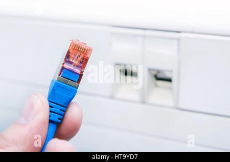 Hand holding ethernet cable. Socket installation RJ45 in background Stock Photo