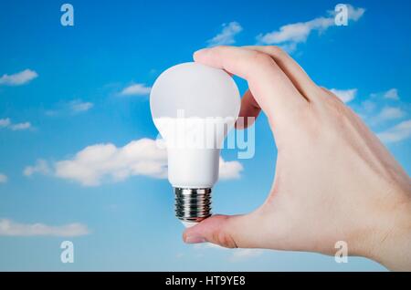 Hand holding LED bulb on sky with cloud background Stock Photo