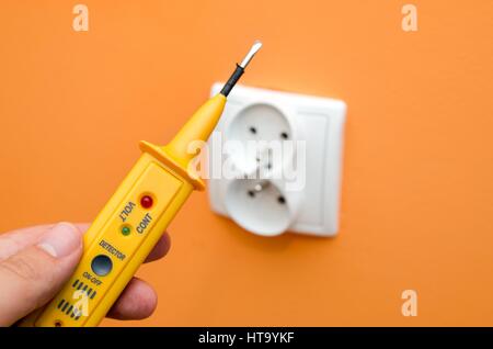 Electricity current meter, turn-screw near to the socket on orange wall. Stock Photo