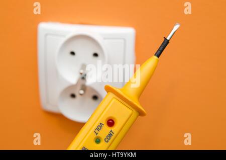 Electricity current meter, turn-screw near to the socket on orange wall. Stock Photo