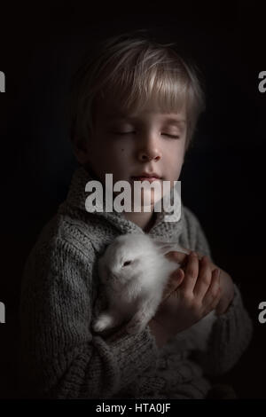 A little boy holding a white rabbit and closing his eyes Stock Photo