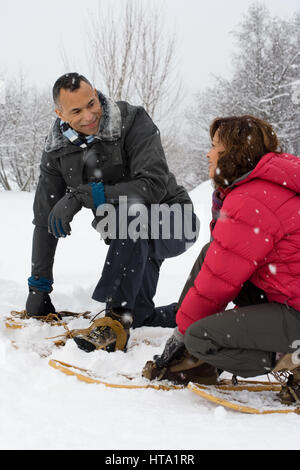 Couple crouching in the snow wearing snowshoes Stock Photo
