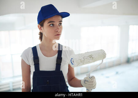 Female in uniform holding roller in white paint Stock Photo