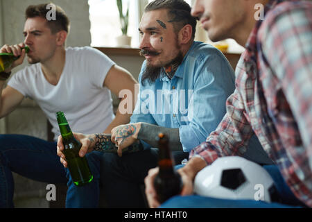 Friends with bottles of beer spending leisure in front of tv set Stock Photo