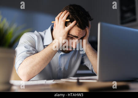 Frustrated man looking at laptop display with his head in hands Stock Photo