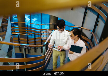 Young Middle Eastern manager going up the stairs of modern office building with his Asian colleague discussing details of documents and statistics in  Stock Photo