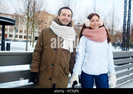 Happy young dates in winterwear looking at camera on skating rink Stock Photo