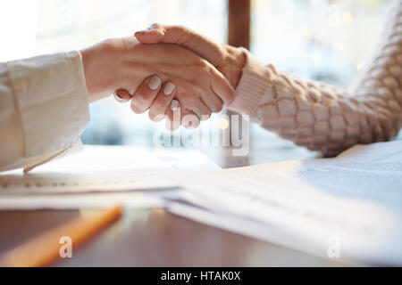 Closeup of two unrecognizable women shaking hands making deal during business meeting at table in cafe Stock Photo