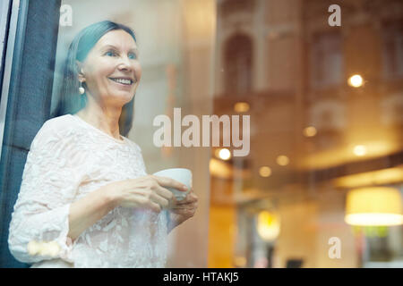Happy woman with cup of tea standing by window in cafe Stock Photo
