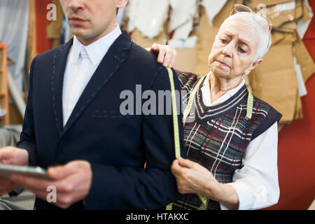 Senior tailor taking measures from jacket sleeve Stock Photo