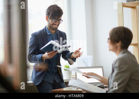 Portrait of two employees, man and woman, talking and smiling standing opposite each other in modern work space Stock Photo