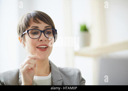 Closeup portrait of young successful businesswoman wearing creative haircut and glasses discussing details of deal with partner via videochat using ha Stock Photo