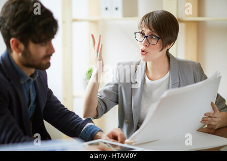 Portrait of two successful business people communicating in office, energetic woman gesturing actively while explaining work plans and documentation d Stock Photo