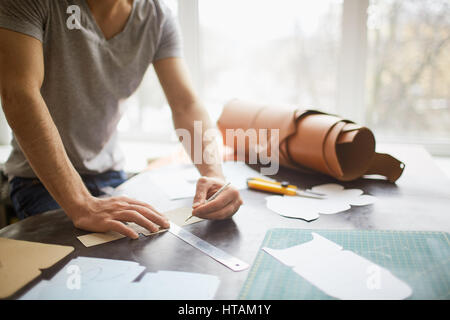 Closeup portrait of unrecognizable leather craftsman working making measupenets in patterns at table in workshop studio Stock Photo