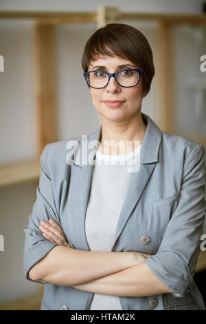 Portrait of young successful businesswoman wearing short haircut and glasses looking confidently to camera with her hands crossed Stock Photo