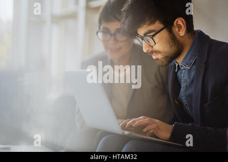 Portrait of two creative business people working together, focus on young middle eastern man wearing beard and glasses busy typing while woman sitting Stock Photo