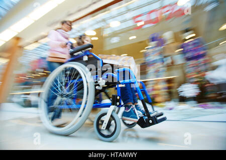 Woman pushing wheelchair with her daughter in the mall Stock Photo