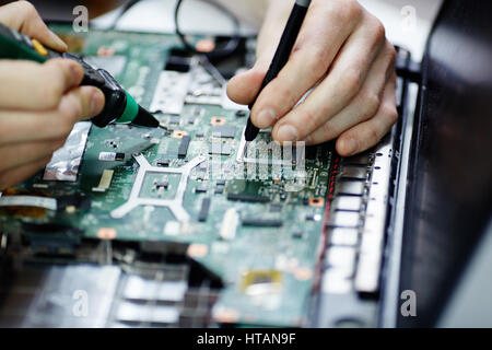 Closeup shot of male hands testing electric current in circuit board of disassembled laptop using multimeter tool on table in maintenance shop Stock Photo