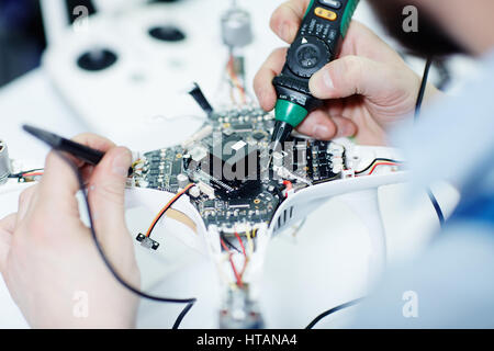 Closeup top view shot of male hands testing electric current in circuit board of disassembled drone using multimeter tool on table in maintenance shop Stock Photo