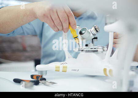 Closeup shot of male hands assembling new surveillance system using quadrocopter drone on table with different tools in modern workshop Stock Photo