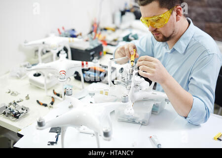 Portrait of modern man setting up new high tech drones and attaching cameras in electronic workshop Stock Photo