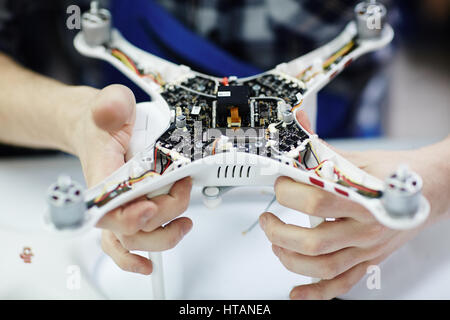 Closeup shot of male hands holding opened drone showing main circuit board and micro controller unit to camera against white table in workshop Stock Photo