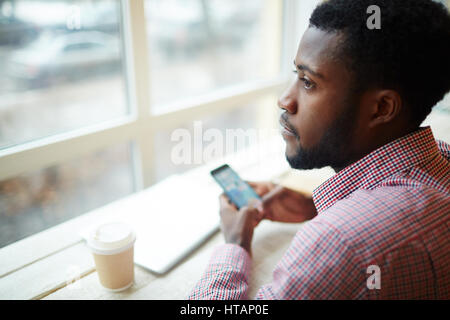 Young entrepreneur with smartphone and drink sitting in cafe Stock Photo