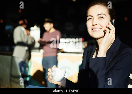 Portrait of successful young businesswoman drinking coffee and bright sunlight and talking by phone smiling happily Stock Photo