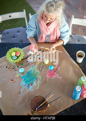 Creative aged woman painitng eggs with special paints Stock Photo
