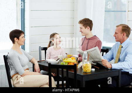Family of four talking by table after breakfast Stock Photo