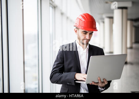 Handsome male engineer is using a notebook for work. The man is a white helmet is looking at the screen with aspiration. Stock Photo