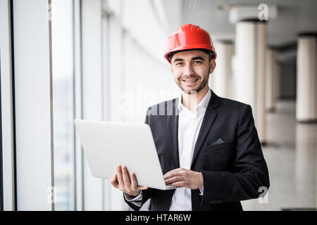 Handsome male engineer is using a notebook for work. The man is a white helmet is looking at the screen with aspiration. Stock Photo