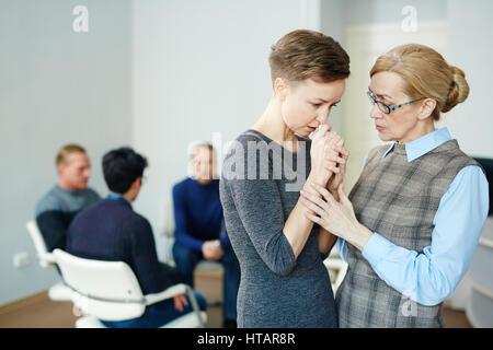 Portrait of mature female psychologist helping young woman to stop crying, overcome  fears and join  group therapy session Stock Photo