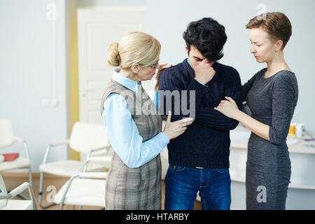 Portrait of mentor and wife comforting young crying man after psychological therapy session Stock Photo