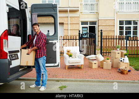 Portrait of smiling man unloading cardboard boxes from transportation van in driveway of his new big house Stock Photo