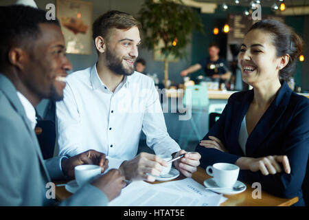 Cheerful co-workers having curious conversation during coffee-break Stock Photo