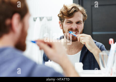 Young man looking in mirror while brushing his teeth Stock Photo