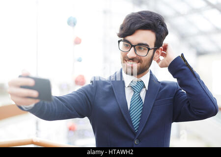 Portrait of modern eastern businessman wearing stylish suit taking selfie using smartphone and smiling Stock Photo