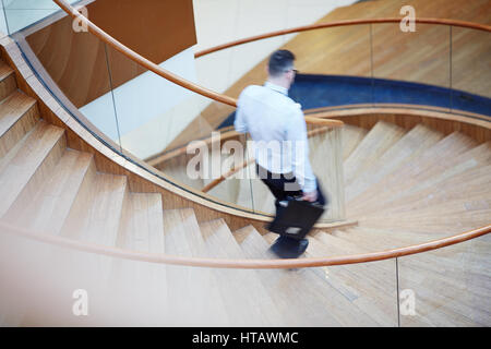 Portrait of unrecognizable blurred businessman going down flight of spiral stairs in modern designer building Stock Photo