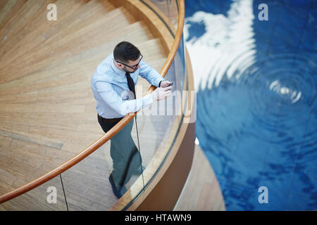 High angle image of modern businessman leaning on railing and typing messages via smartphone in design architectural building Stock Photo