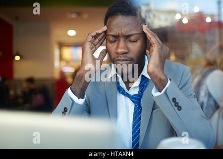 Businessman rubbing his temples suffering from headache while sitting at counter in coffee shop, shot behind glass window Stock Photo