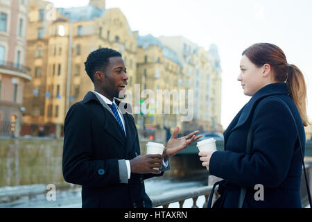 Portrait of two business colleagues leaving office and standing in autumn street by river having conversation and holding disposable coffee cups both  Stock Photo