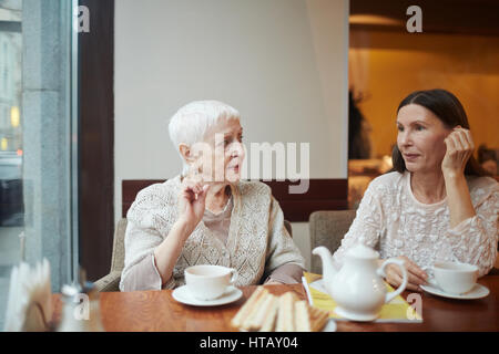 Senior friendly women sitting in armchairs and talking in cafe Stock Photo