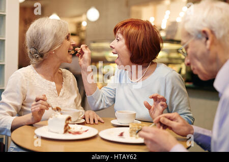 Carefree mature female putting tasty dessert into her friend mouth Stock Photo