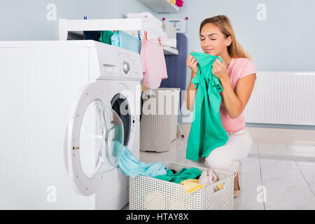 Young Smiling Woman Smelling Clothes After Washing In Washing Machine At Utility Room Stock Photo